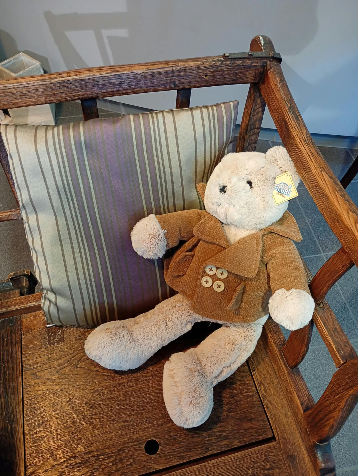 Teddybeer met jasje op een oude houten stoel met gestreept kussen