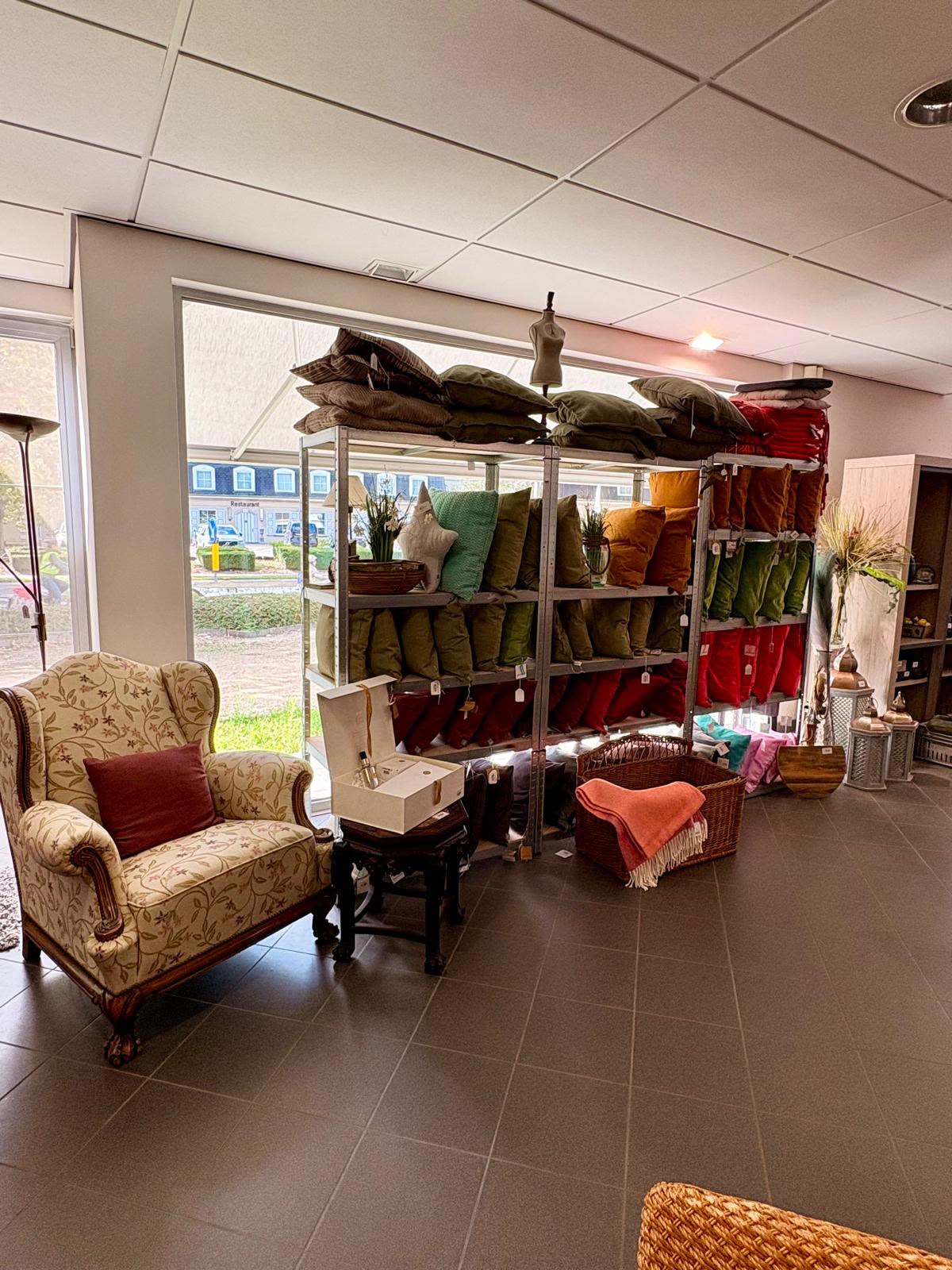 Bloemrijke fauteuil voor een rek met gekleurde kussens in de winkel van Beaushop